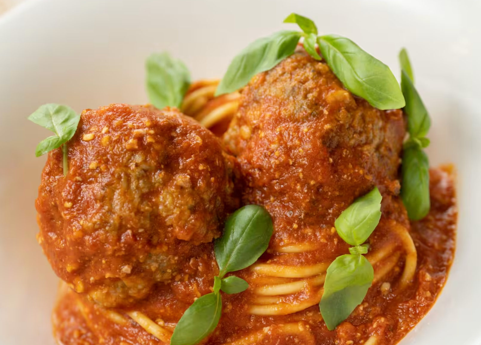 Homemade spaghetti and meatballs topped with fresh basil in a rich tomato sauce on a white plate.