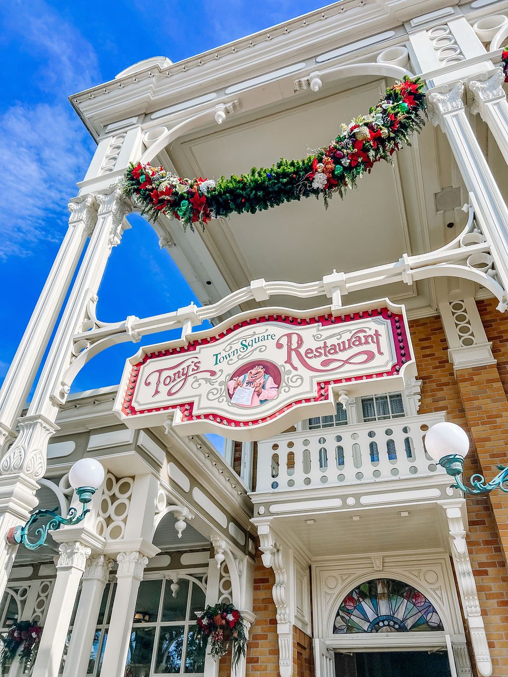 White decorative Victorian-style archway with holiday garland and Plaza Restaurant sign at Disney World's Main Street USA.