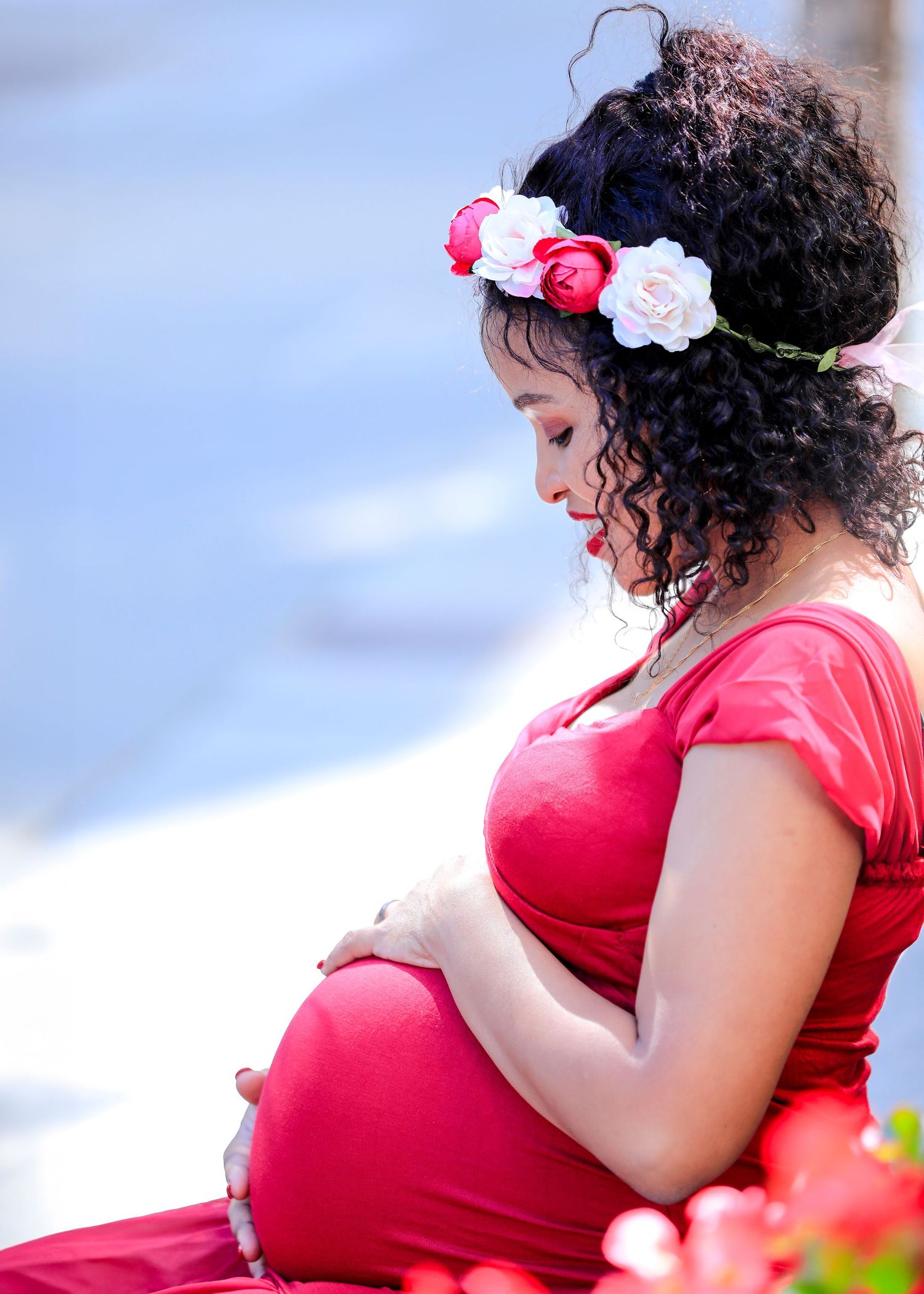 Expectant mother wearing red dress and floral crown looks down at baby bump.