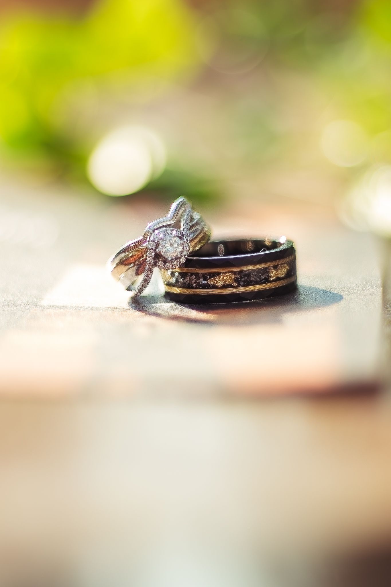 Wedding rings with a diamond engagement ring and dark wooden band captured with soft bokeh background.
