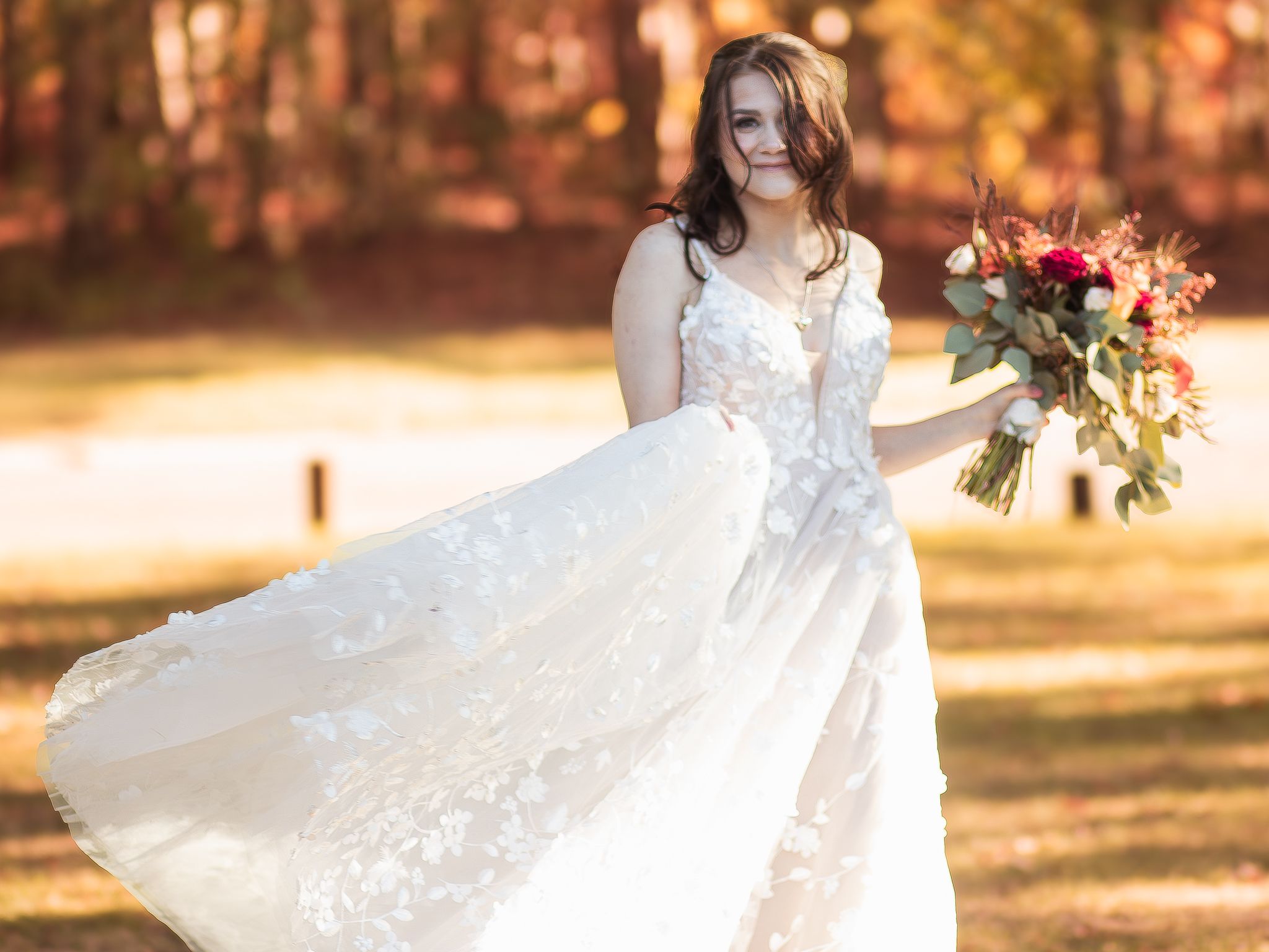 A white lace wedding gown flows in the breeze as the bouquet features vibrant fall flowers in golden sunlight.