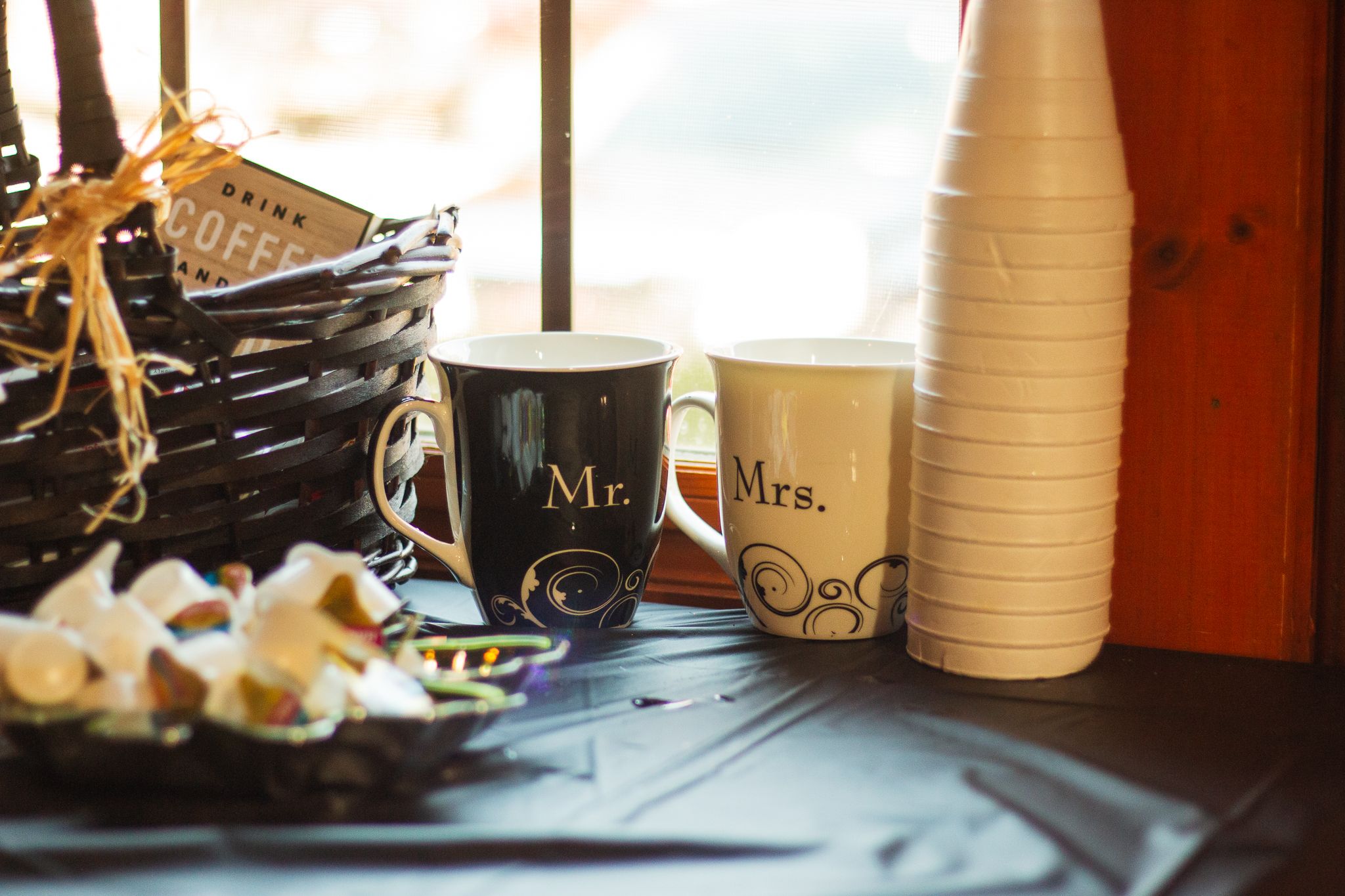 Coffee cups and drink containers arranged on a rustic table with a basket in warm ambient lighting.