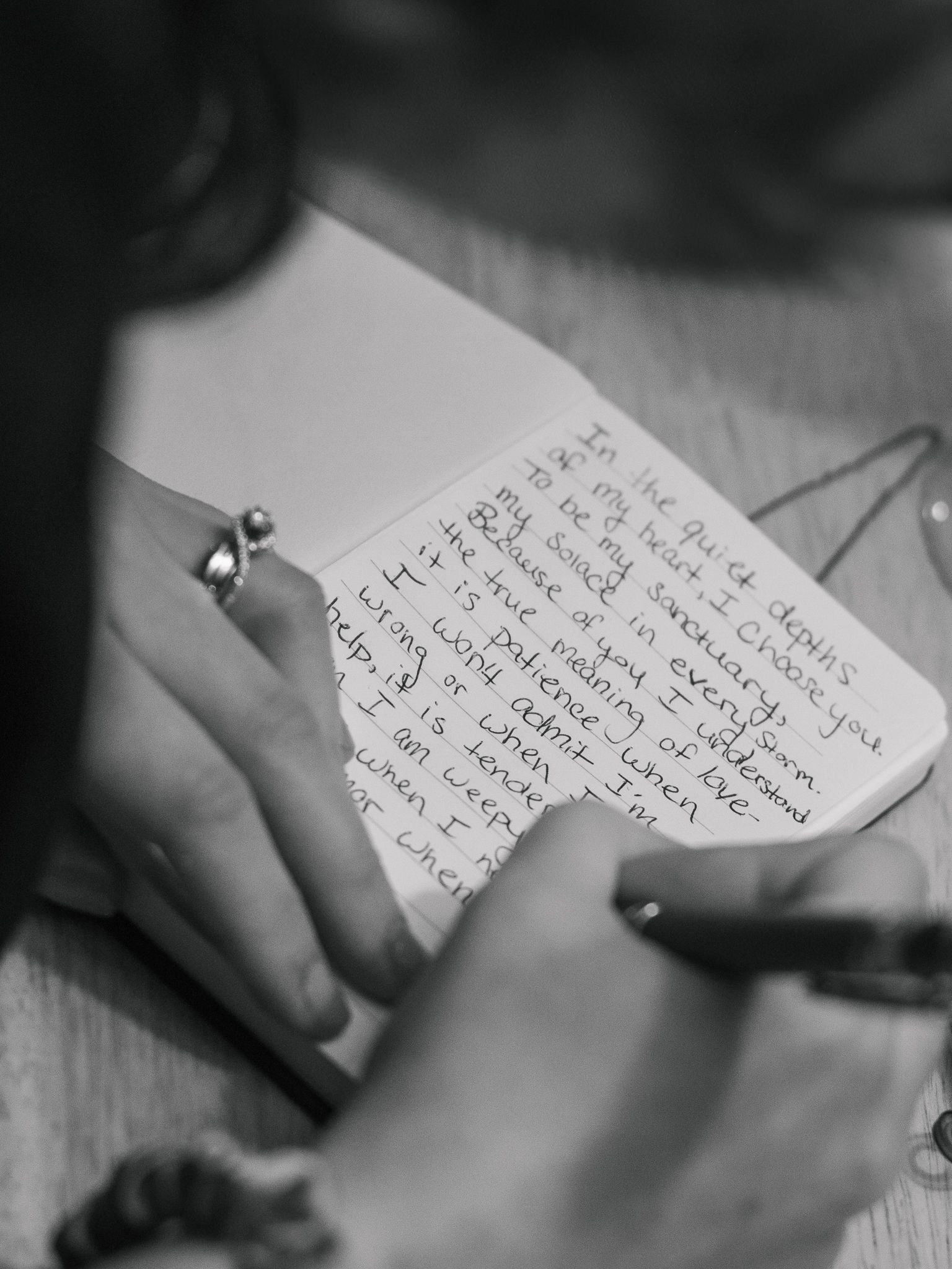 Close-up black and white photo of hands writing on paper with handwritten text visible.