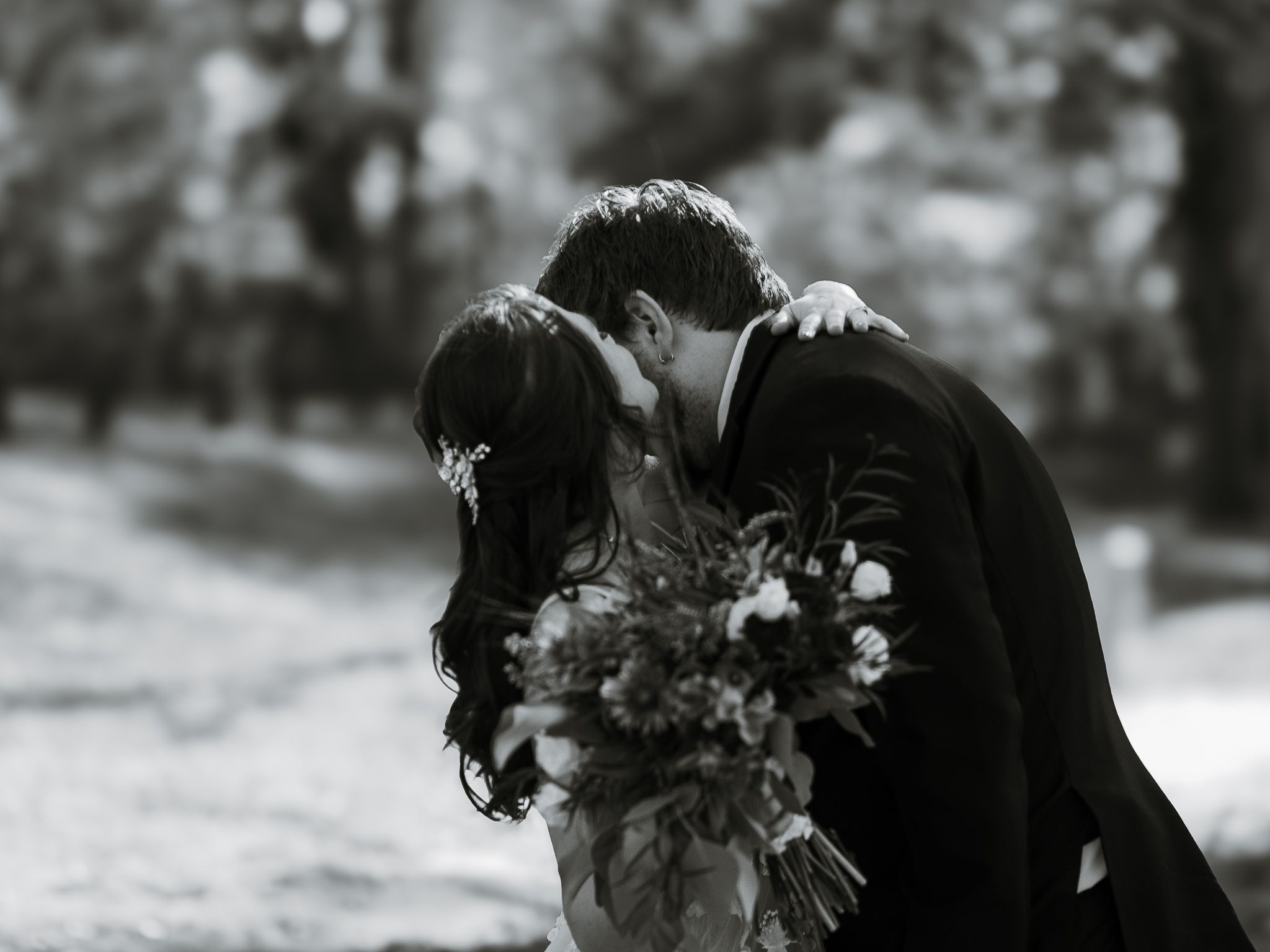 A romantic black and white wedding photo showing a couple embracing while the bride holds a floral bouquet.