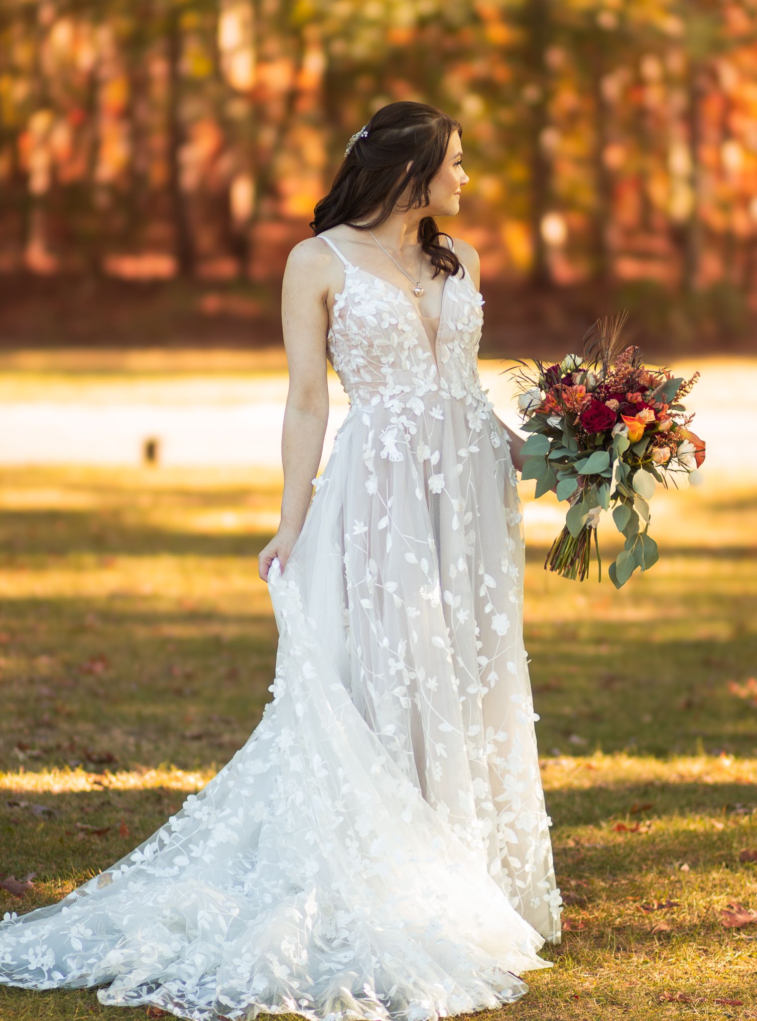Beautiful wedding dress with floral appliques and flowing train captured in golden autumn light with colorful bouquet.
