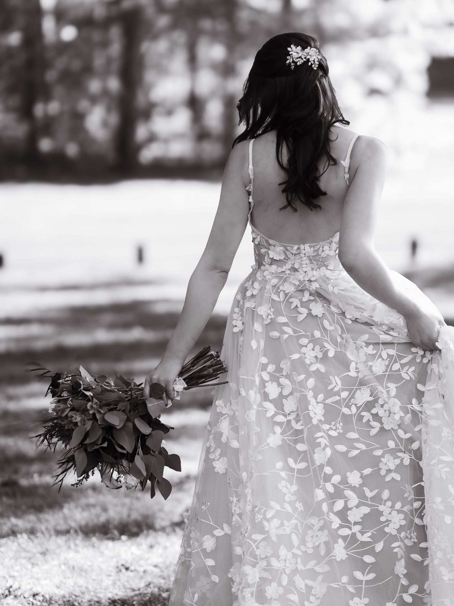 Black and white photo of a bride from behind showing intricate lace wedding dress details and holding a bouquet.