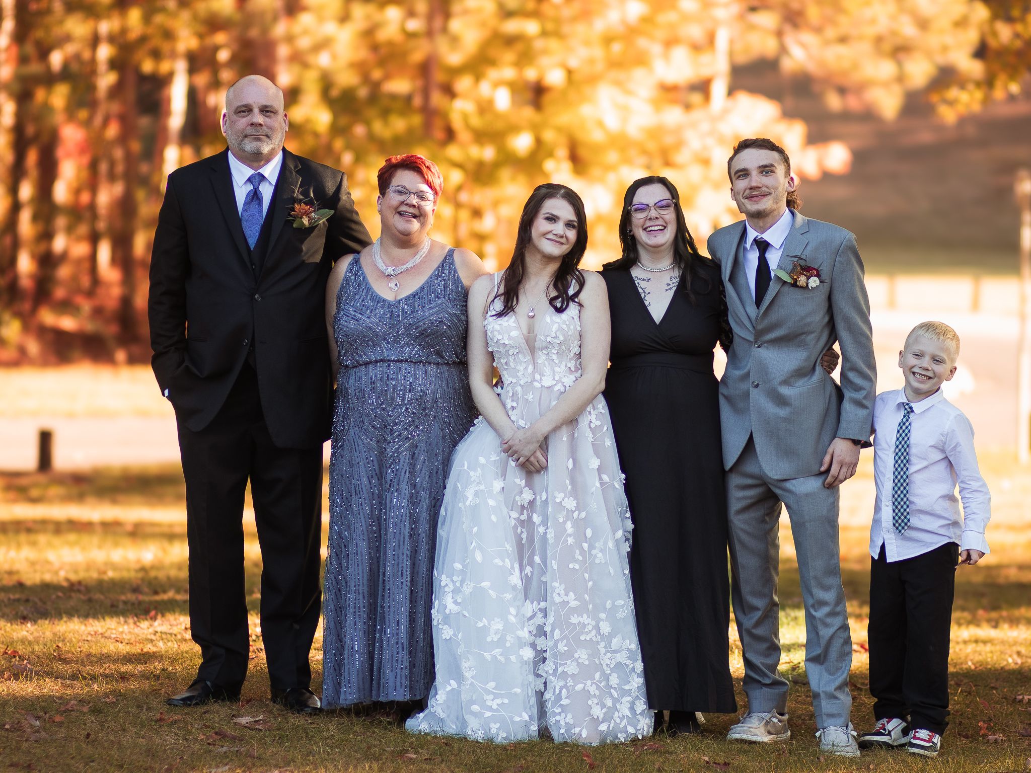 Wedding party poses together on autumn day with golden fall foliage in background.