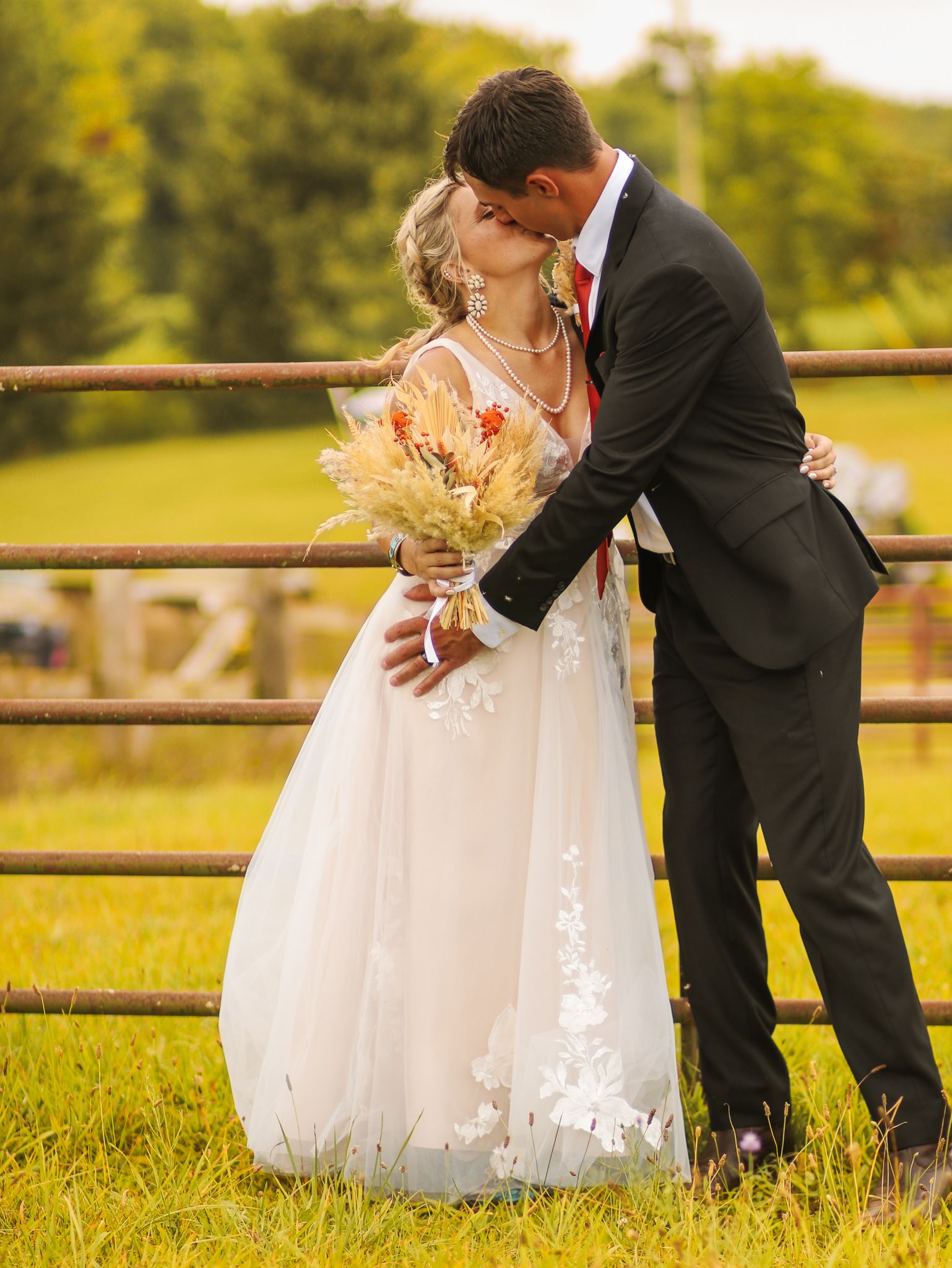 Romantic wedding moment captured against rustic fence in golden field setting.