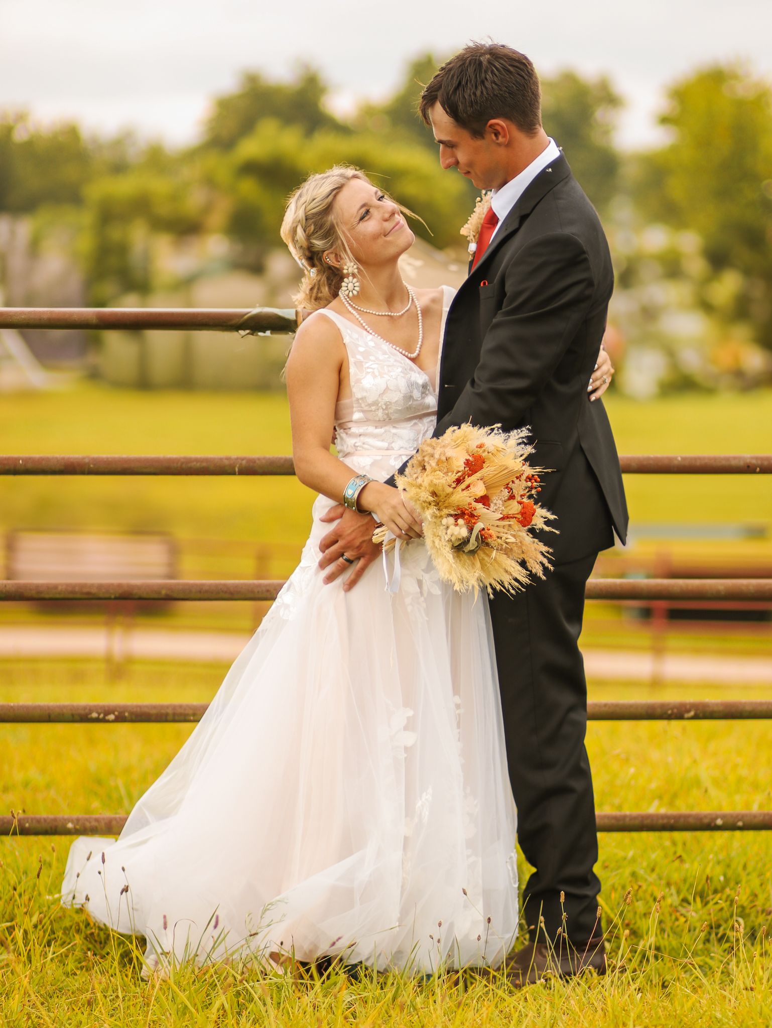 Intimate wedding portrait in front of rustic fence with peach floral bouquet.