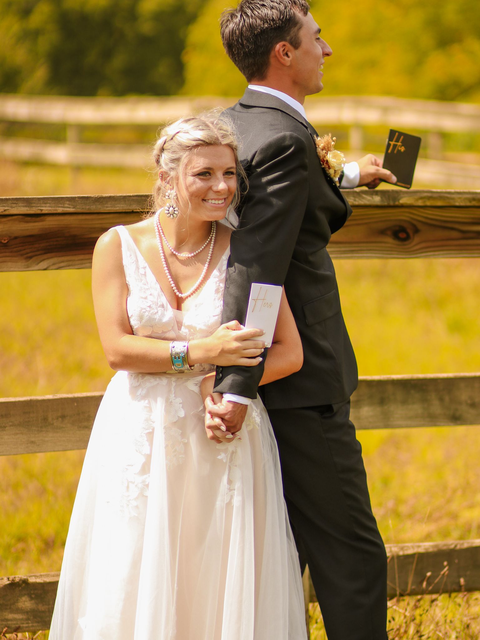 Couple in wedding attire standing back-to-back at rustic wooden fence during first look photos.