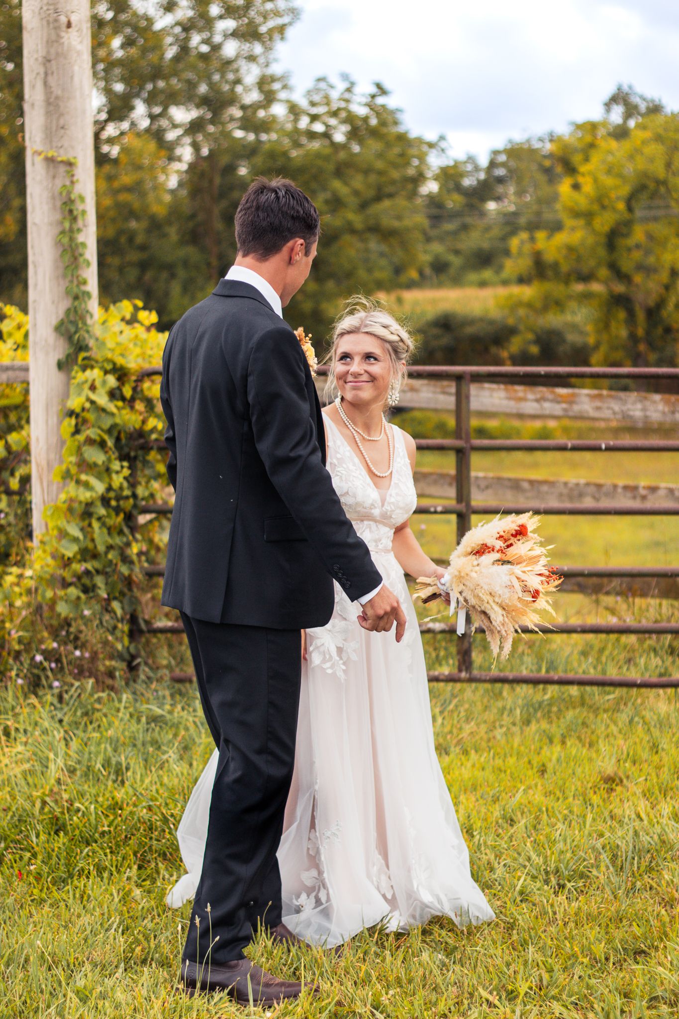 Wedding couple sharing tender moment by wooden fence in countryside setting.
