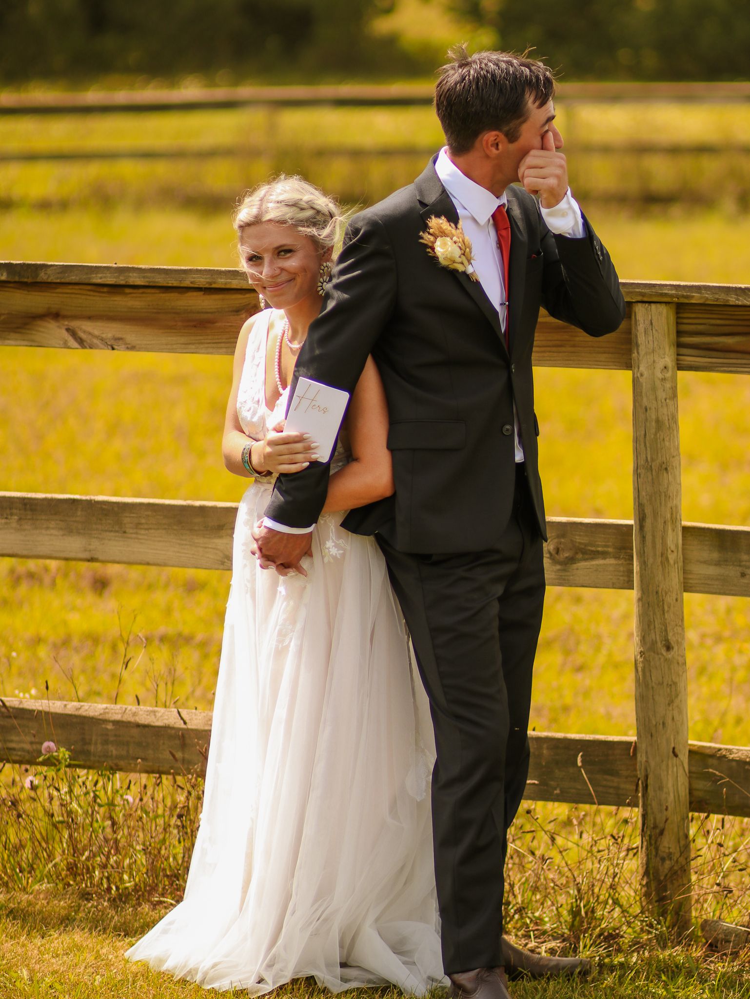 Wedding couple shares emotional first look moment at wooden fence in autumn field setting.