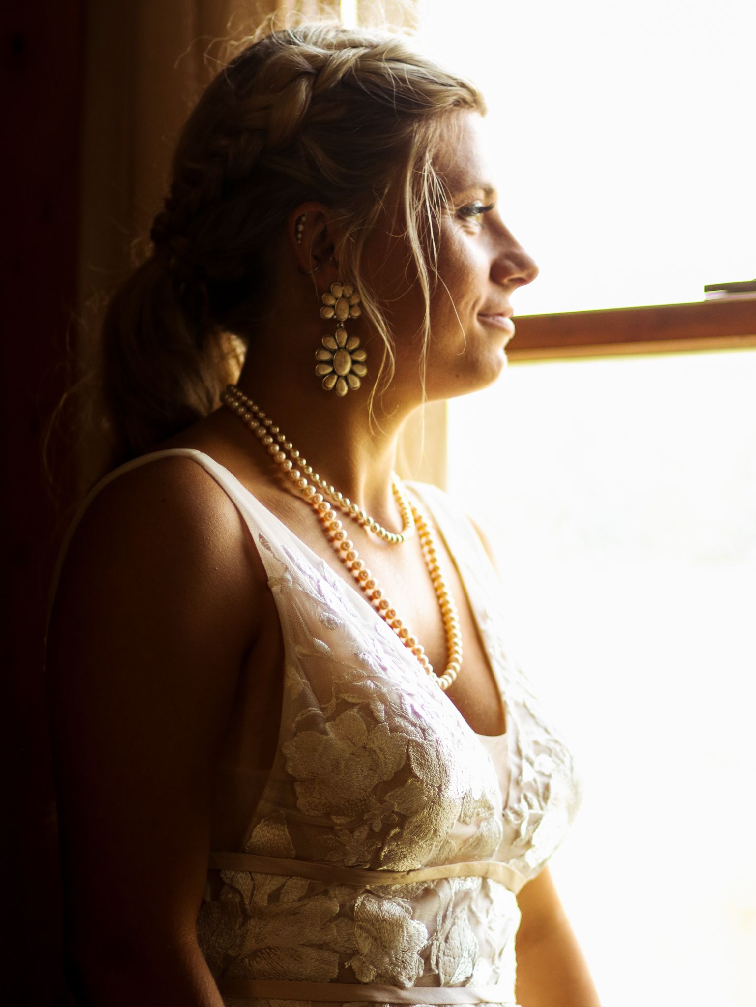 Wedding attire portrait in silhouette near window with pearl jewelry details.