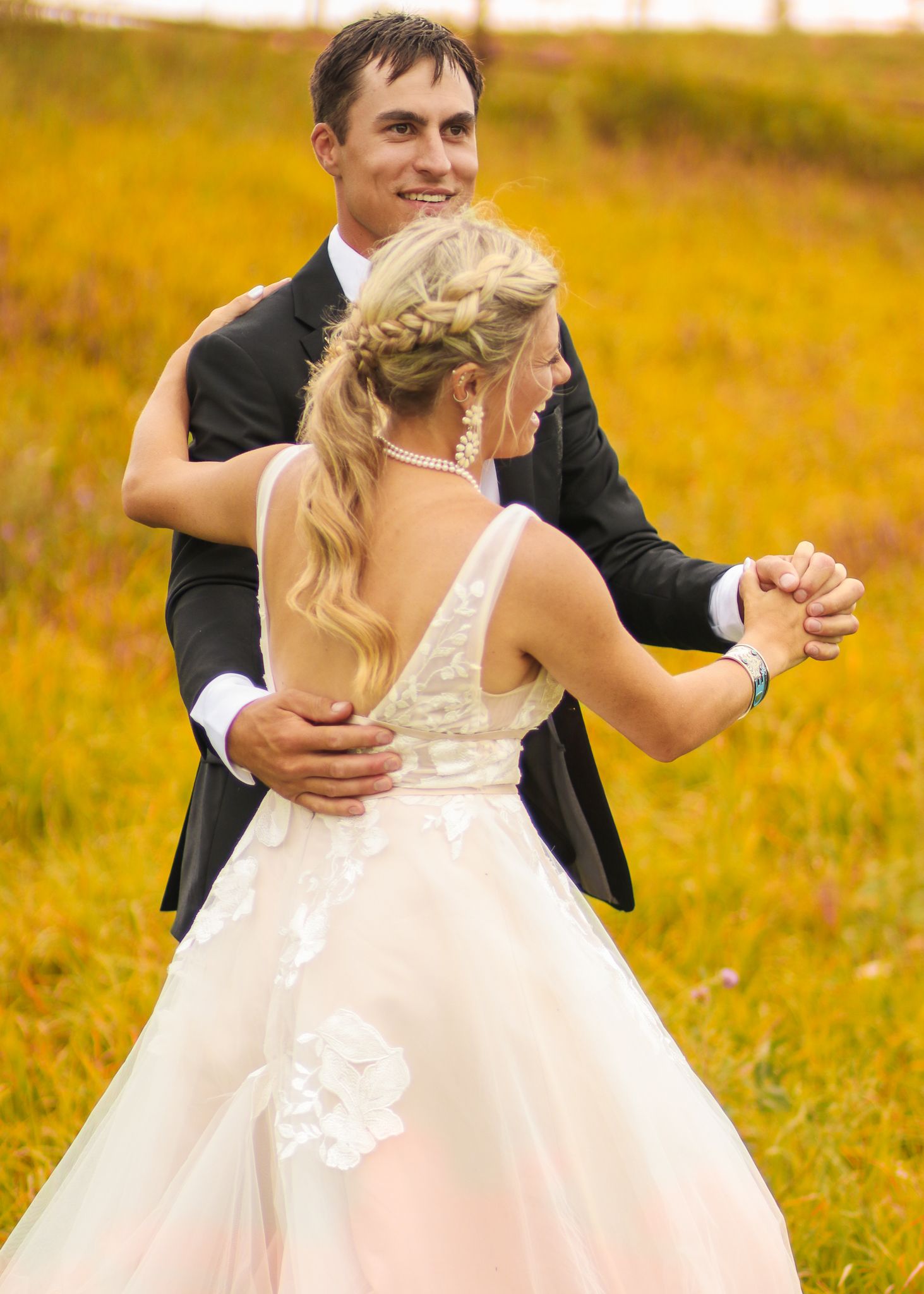A couple dances together in a sunlit field wearing elegant wedding attire.