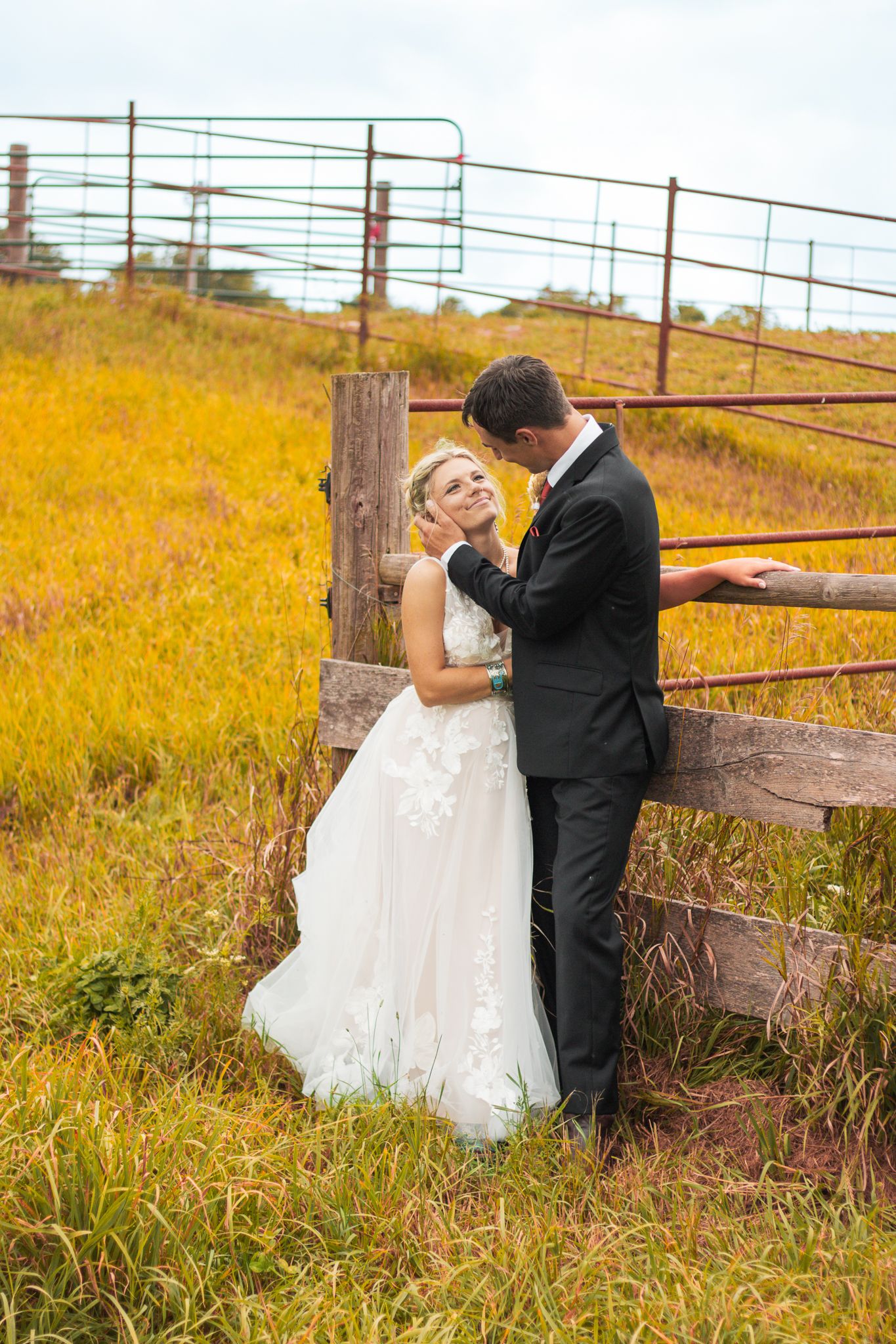 A romantic wedding moment captured by a rustic fence in an autumn field.
