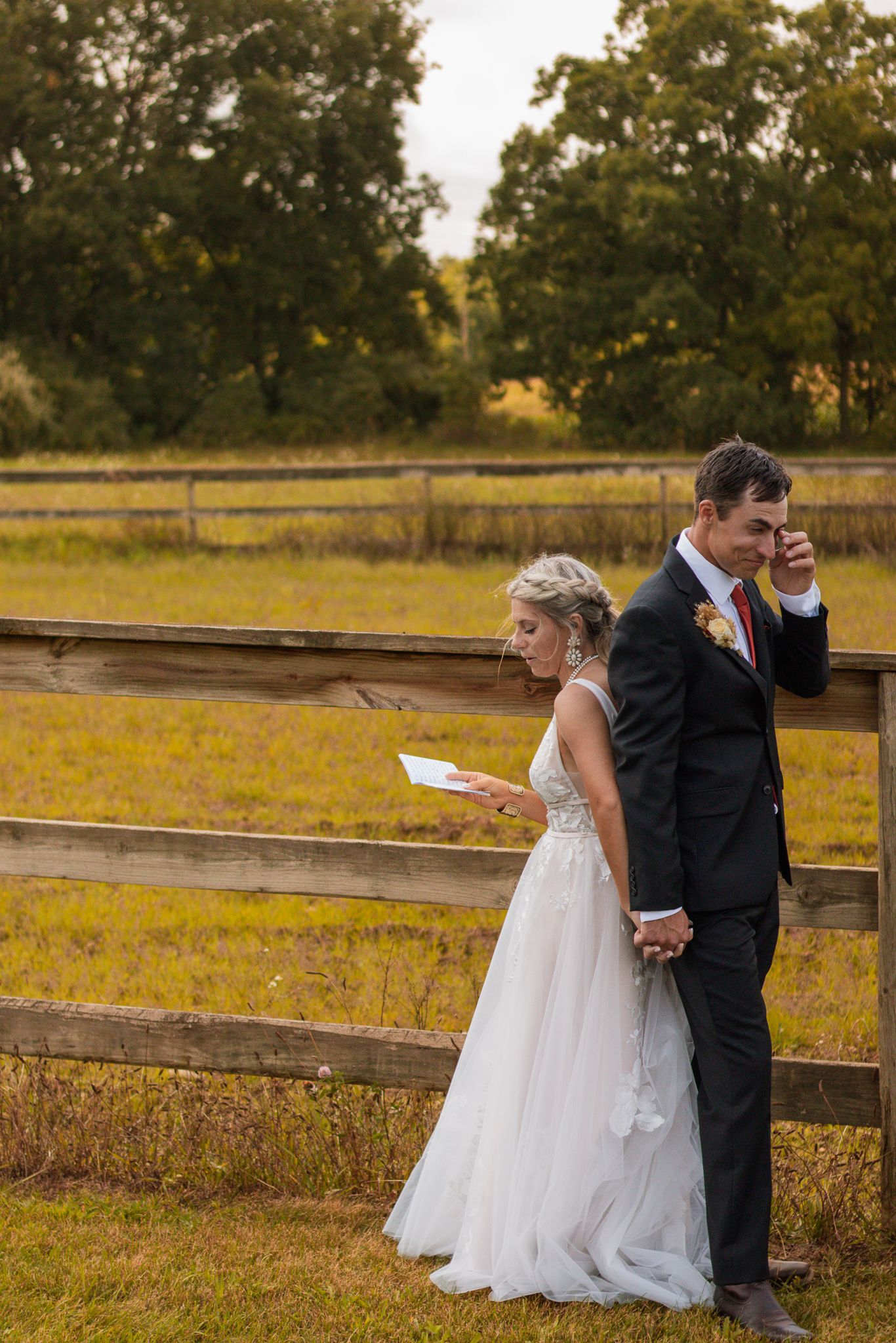 A couple shares an intimate first look moment against a rustic fence surrounded by autumn foliage.