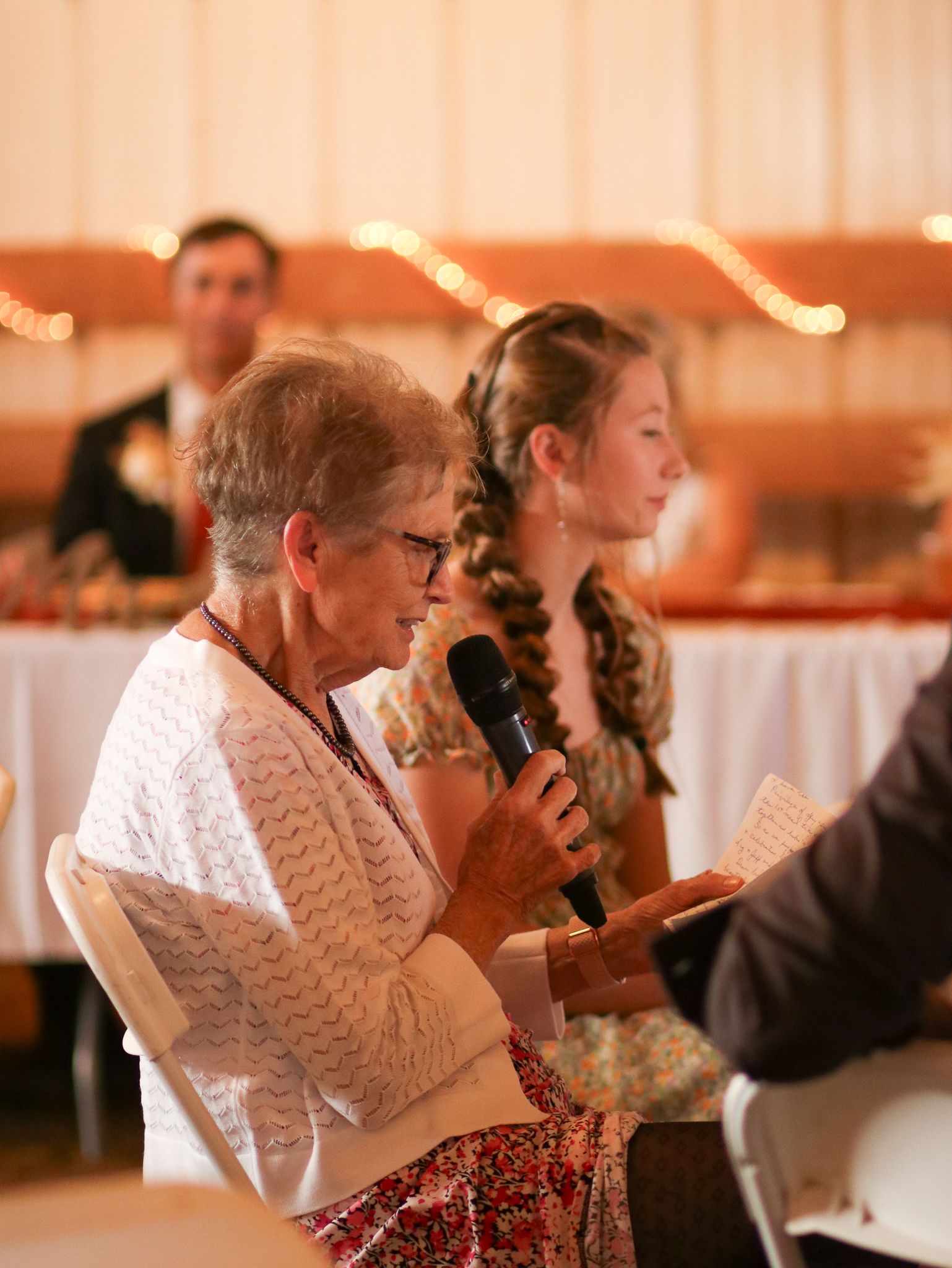 Wedding reception moment with speaker holding microphone and reading from paper.