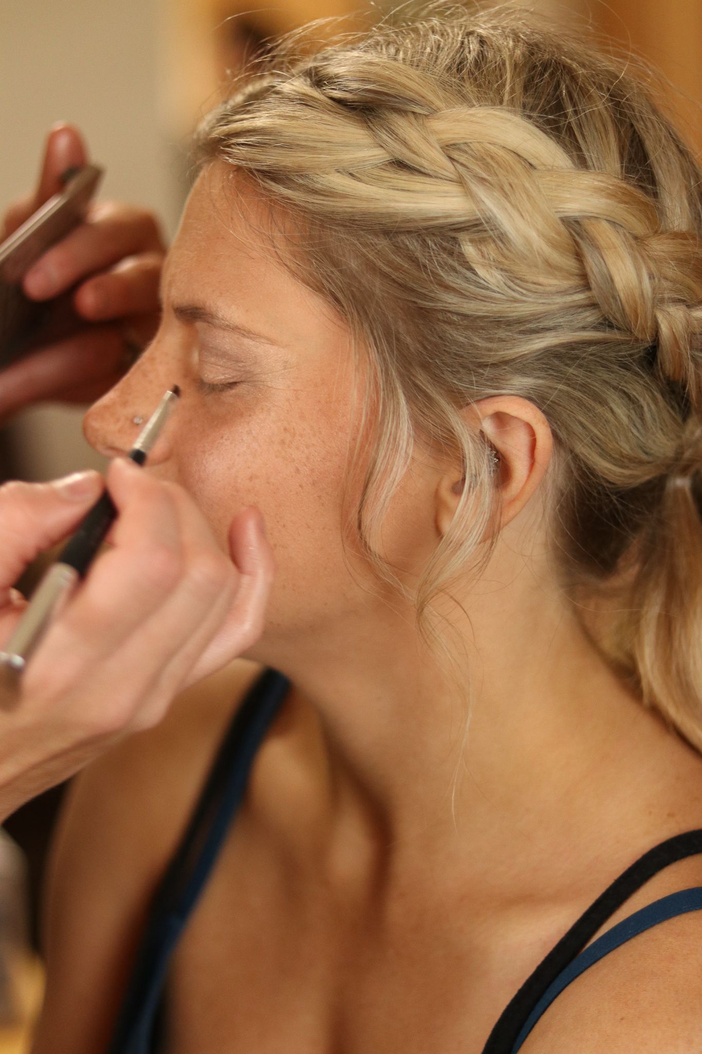 Makeup artist applying cosmetics with a brush during a beauty session with braided blonde hairstyle.