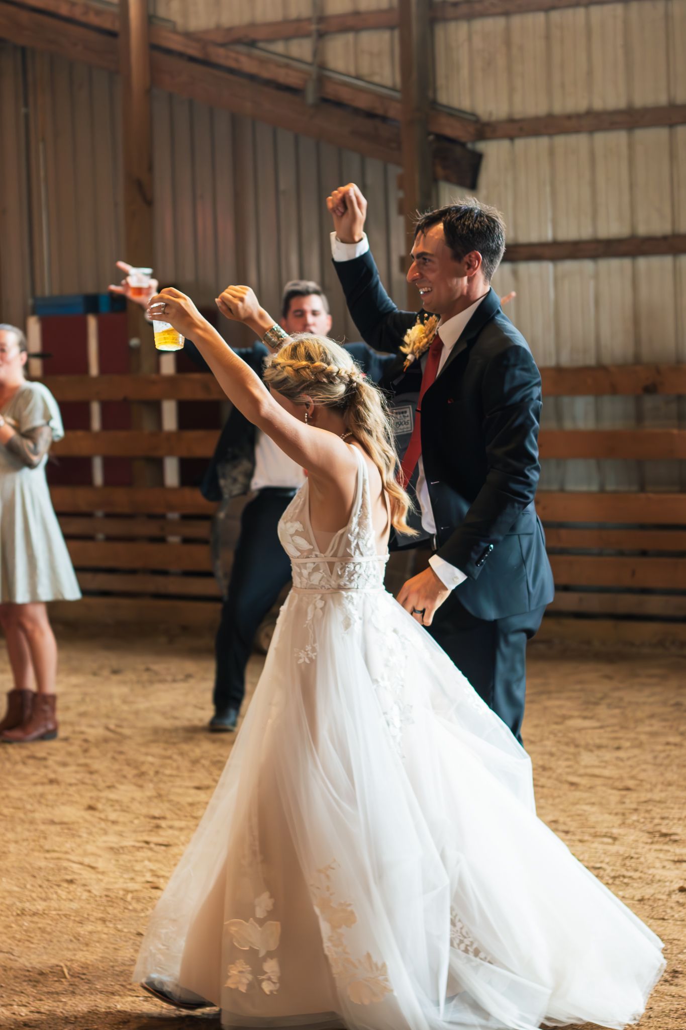 Wedding couple dances energetically in a rustic barn setting.