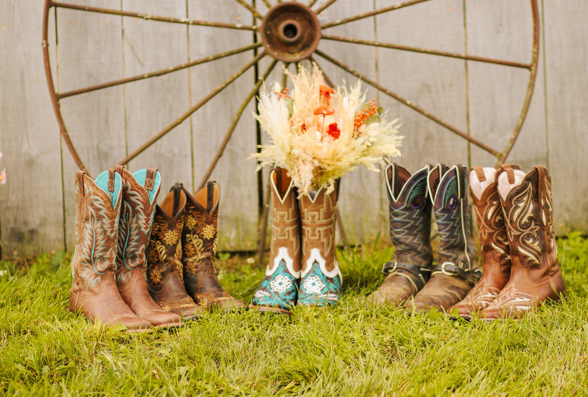 Collection of western cowboy boots arranged with a wagon wheel and floral decorations for a rustic wedding.