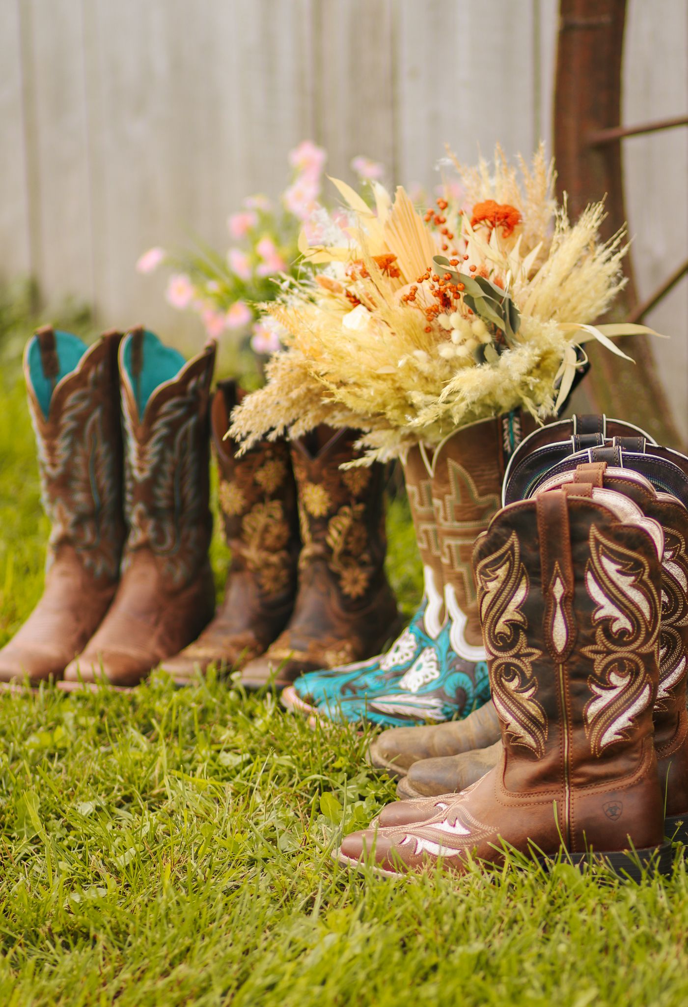 Rustic display of cowboy boots with turquoise accents alongside dried flower arrangements on grass.