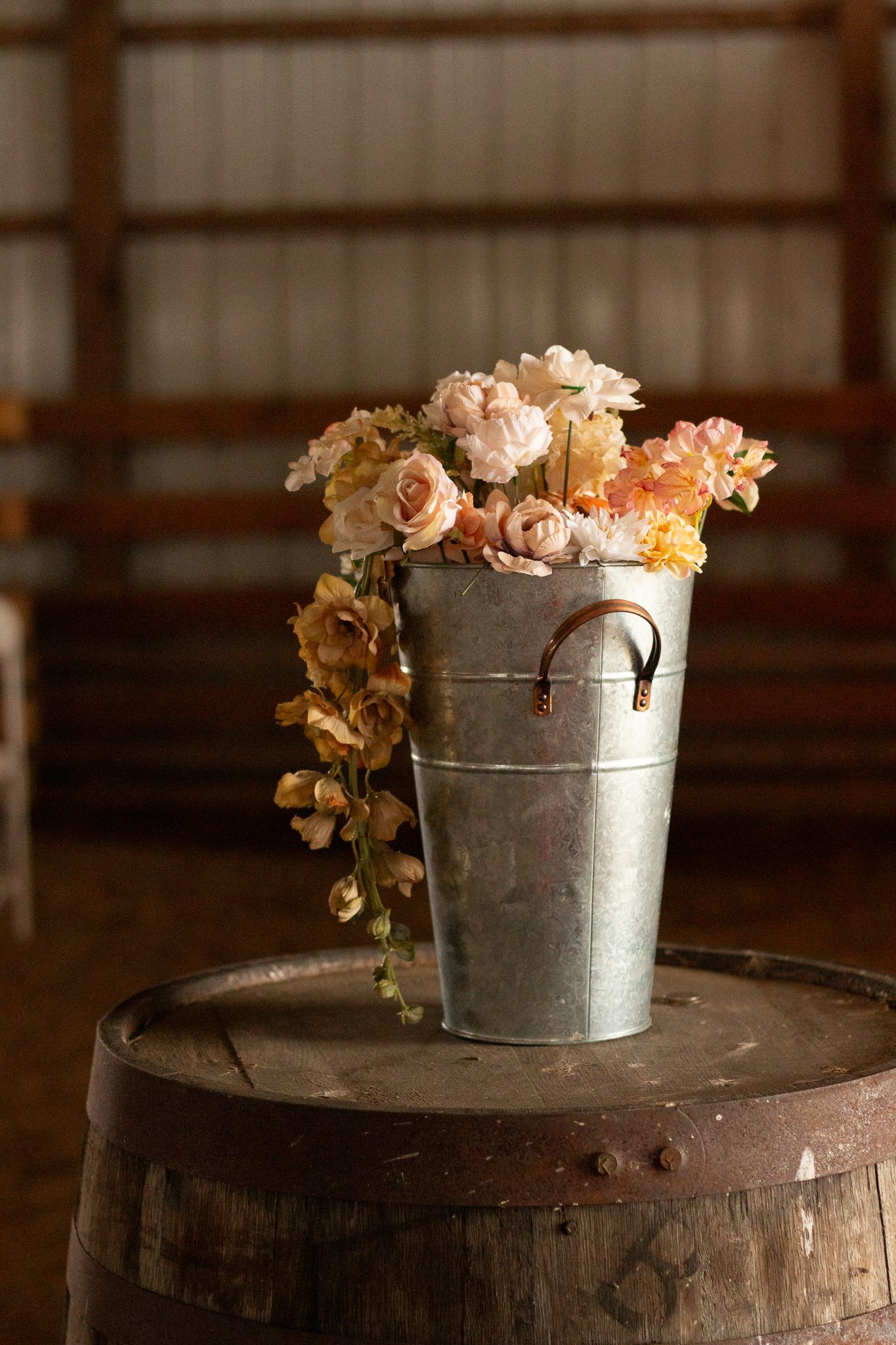 Vintage galvanized metal bucket filled with peach and cream roses atop a wooden barrel.