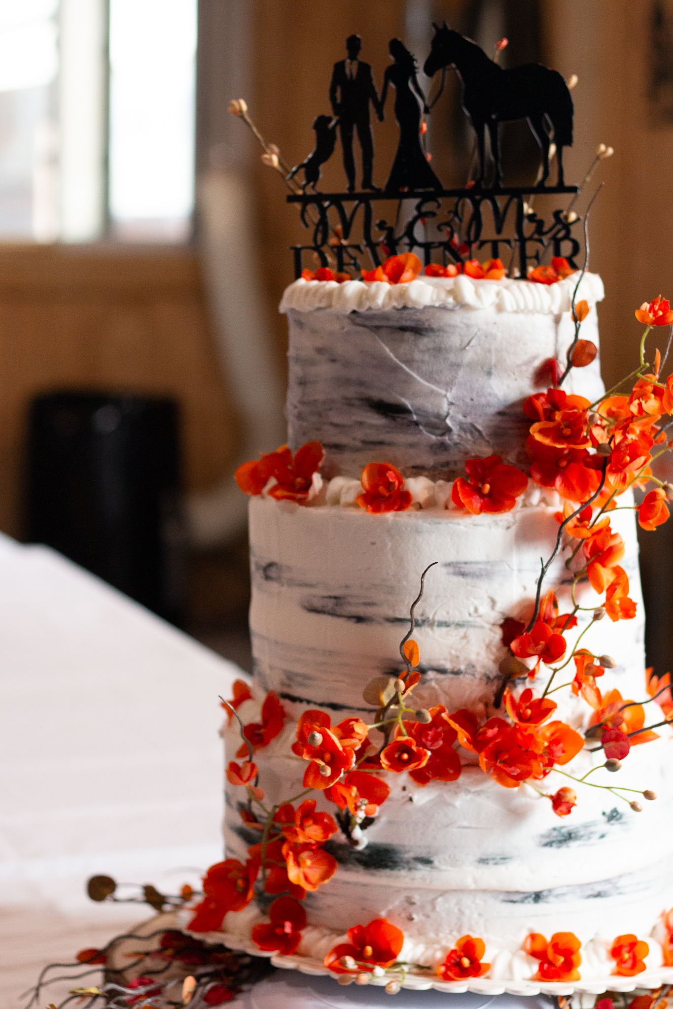 Three-tiered white wedding cake decorated with cascading orange flowers and a silhouette topper.