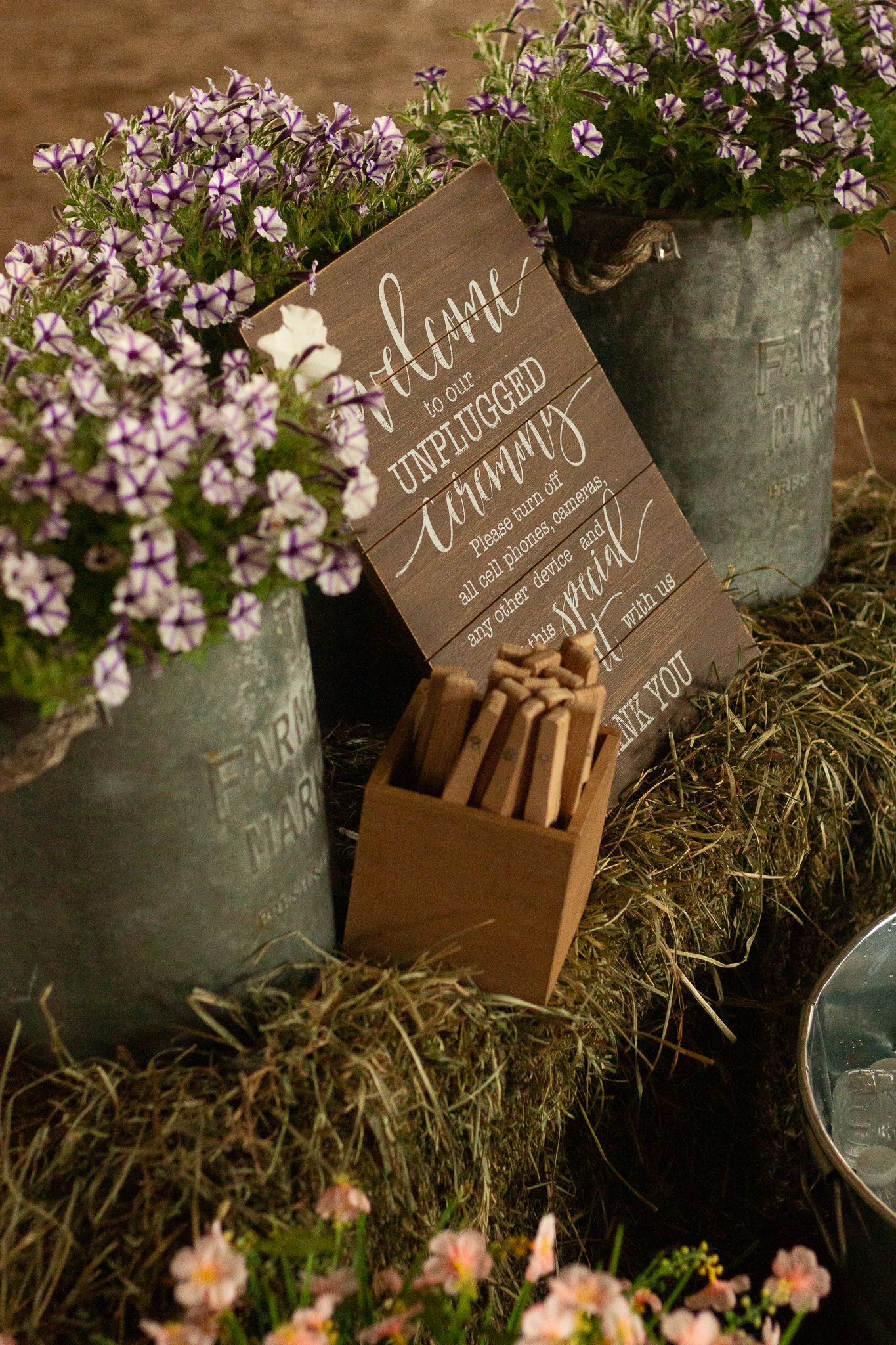 Wooden wedding sign with calligraphy displayed among potted flowers and hay bales.