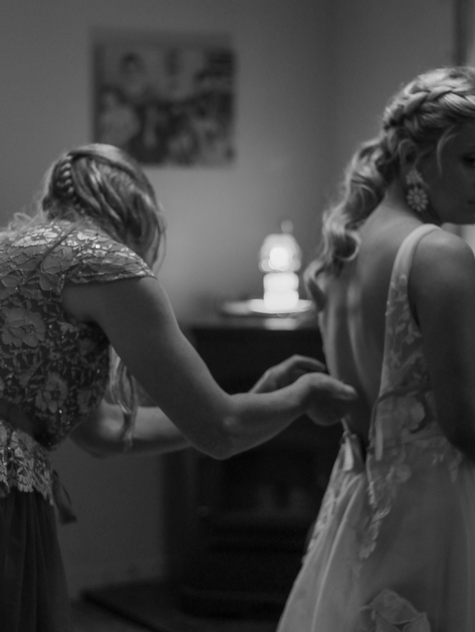 A black and white image showing the back of a wedding dress being fastened in preparation.