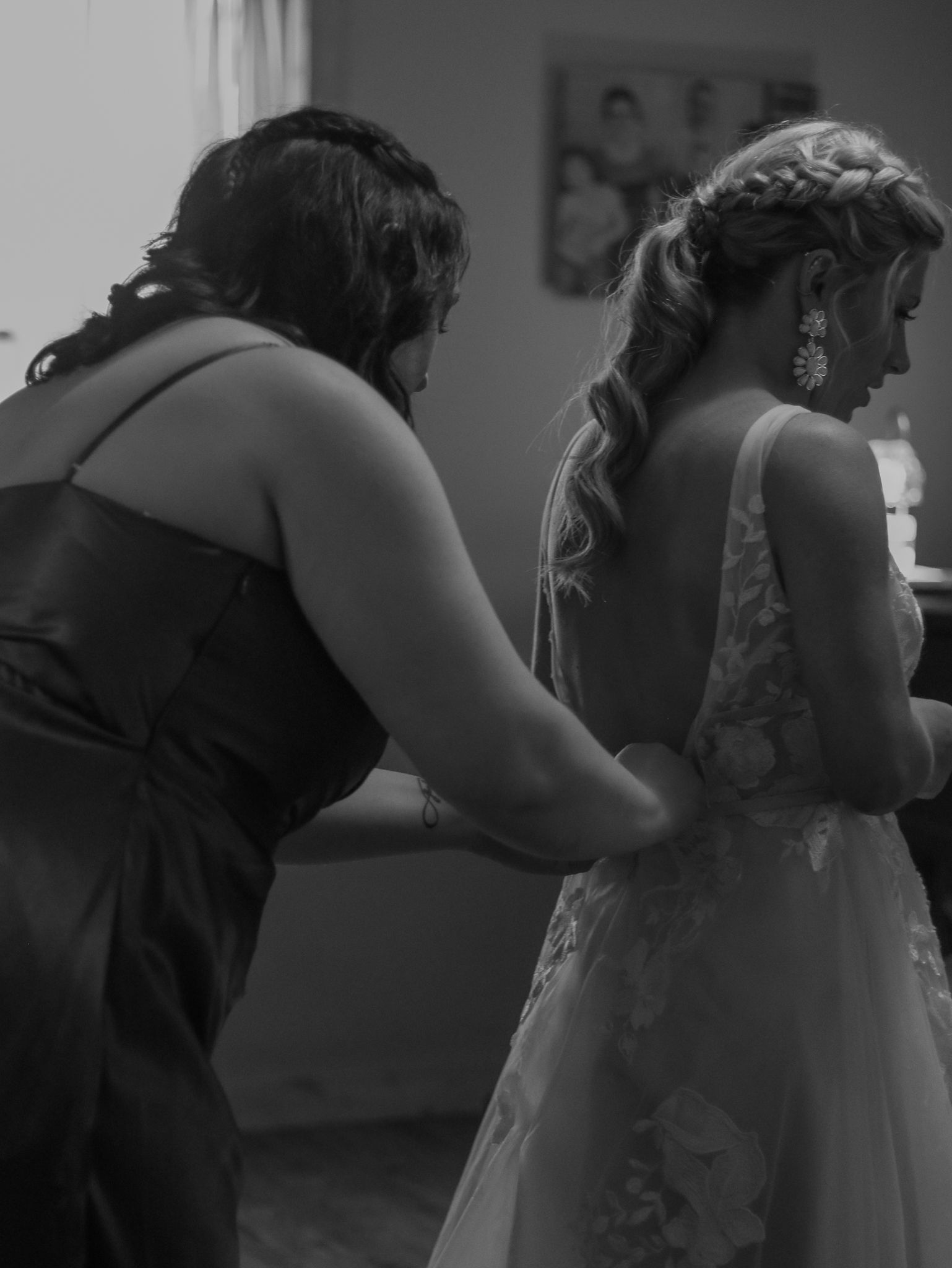 A candid black and white photo of dress adjustments during wedding preparations.