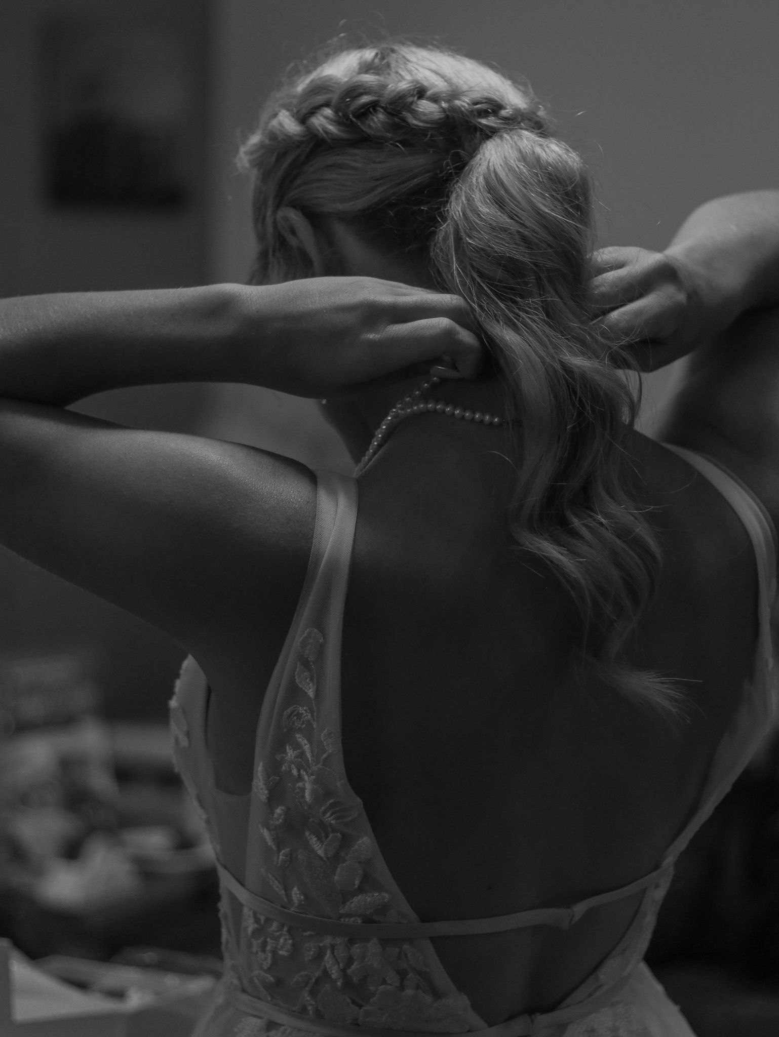 Artistic black and white photo showing intricate back detail of a wedding dress during preparations.