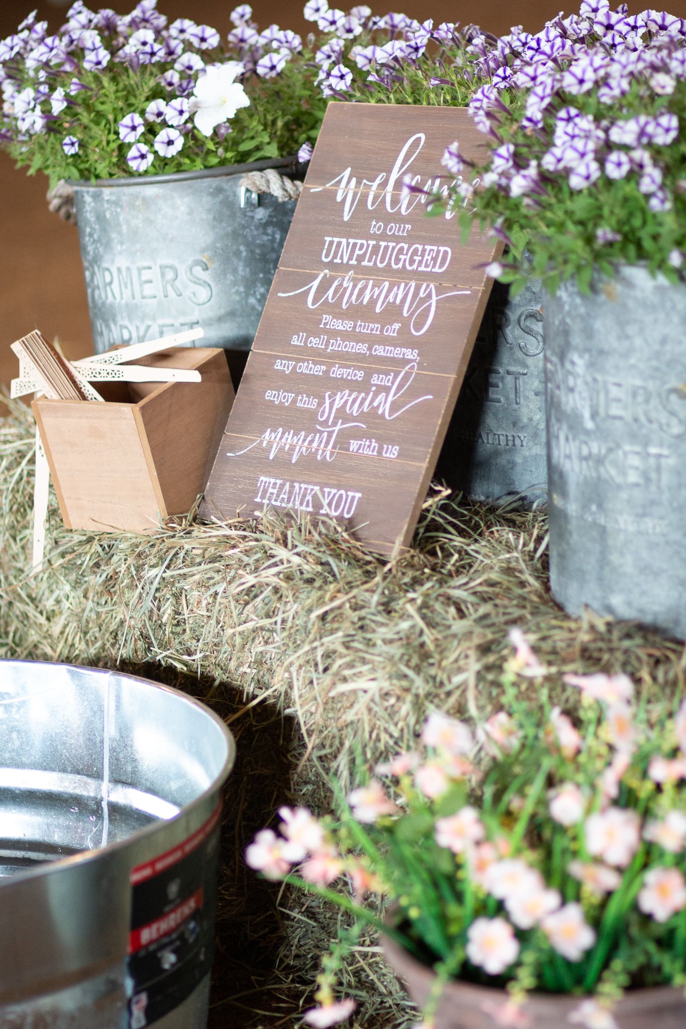 Rustic wedding decor featuring galvanized buckets with purple flowers and wooden welcome sign.