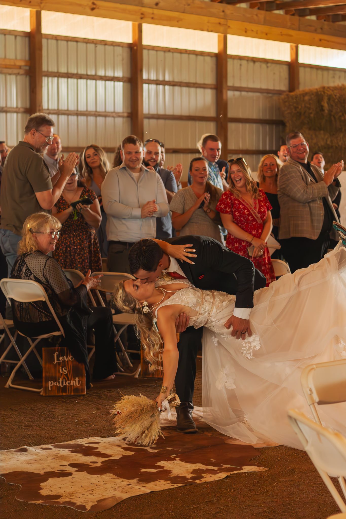 A couple performs a romantic dip on a wooden floor at their rustic barn wedding reception while guests cheer.