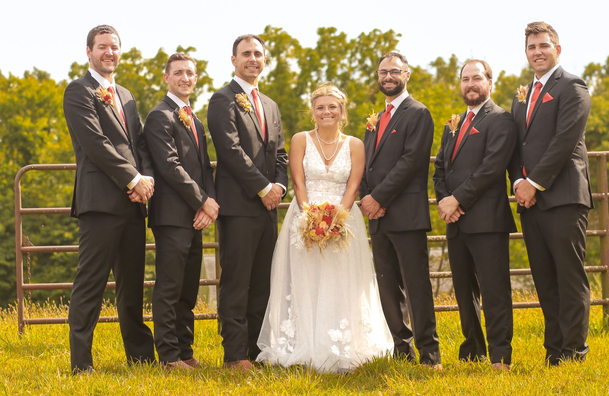 Wedding party poses together outdoors against a nature backdrop on a sunny day.