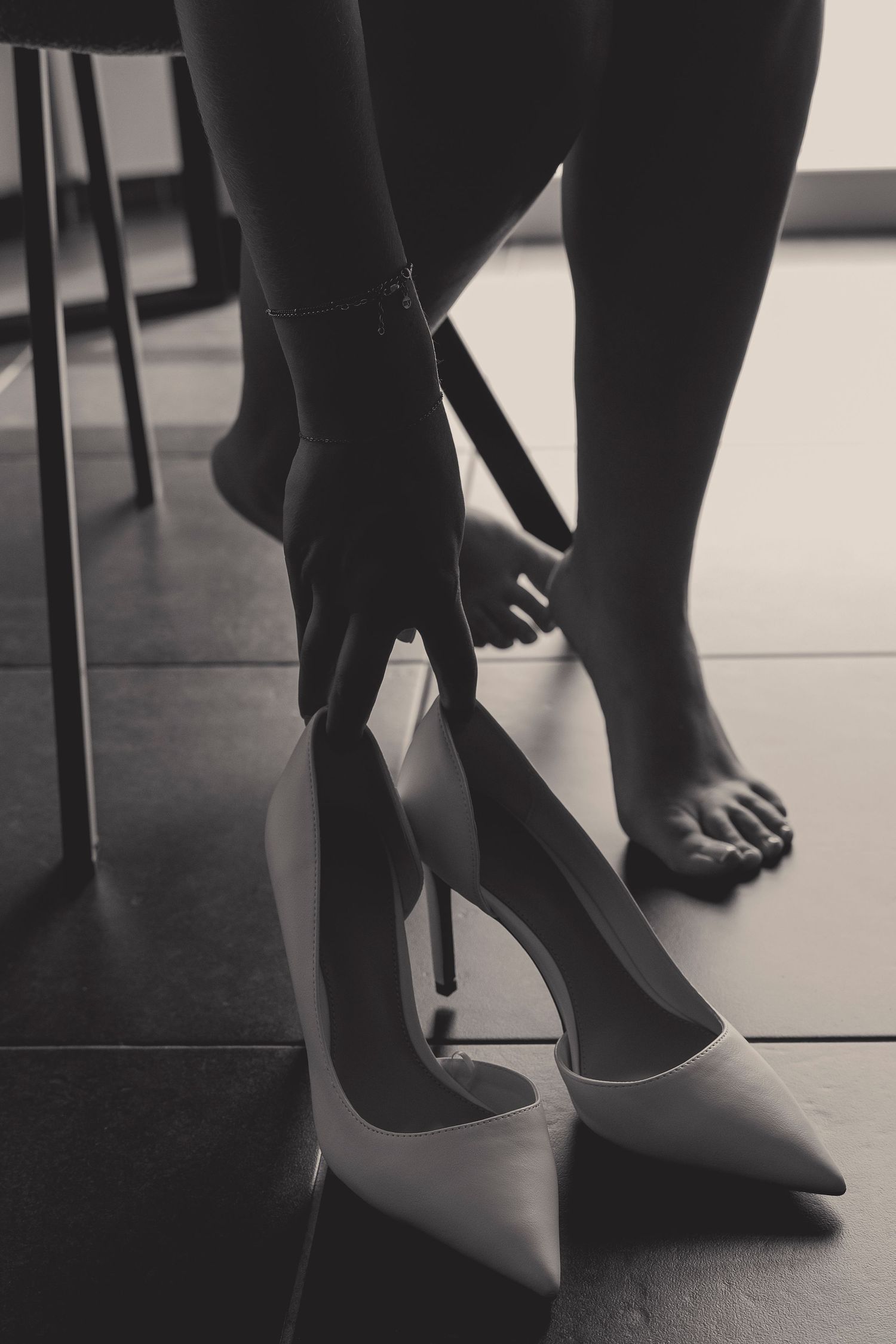 Black and white image of feet and hands putting on white high heel shoes.
