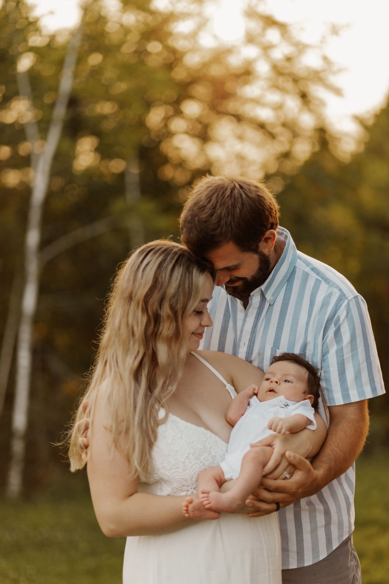 A couple holding their newborn baby outdoors during golden hour sunset in summer.