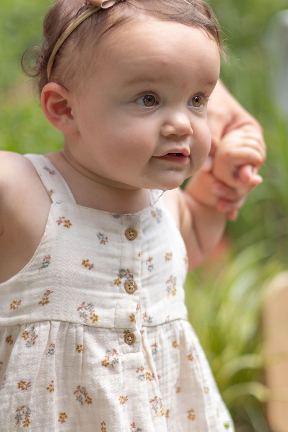 A small child in a floral dress smiles while playing outdoors in natural lighting.