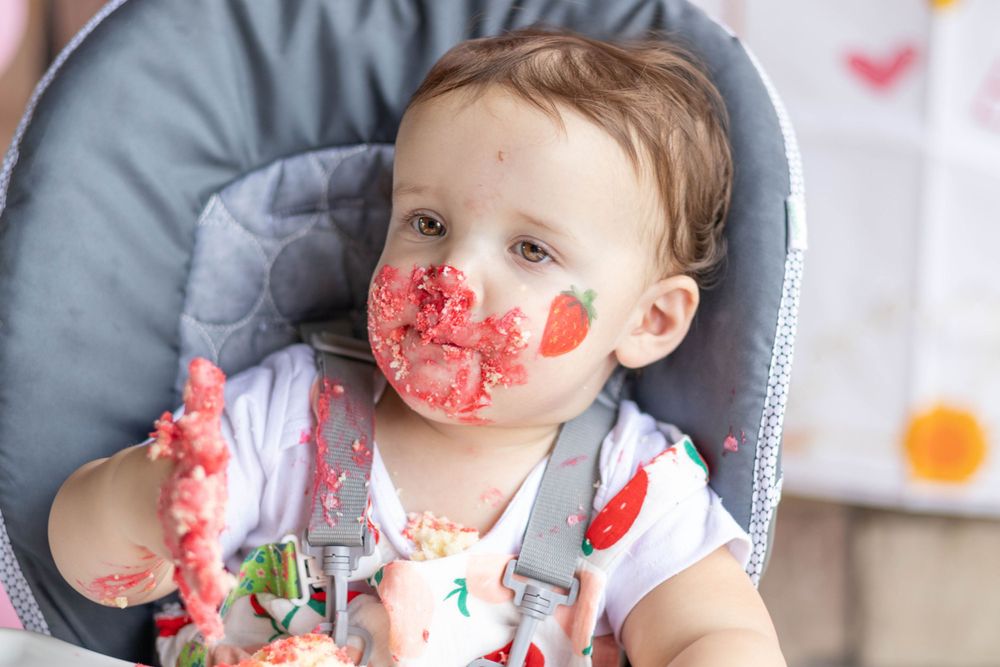 Baby in highchair with face covered in red watermelon or cake.