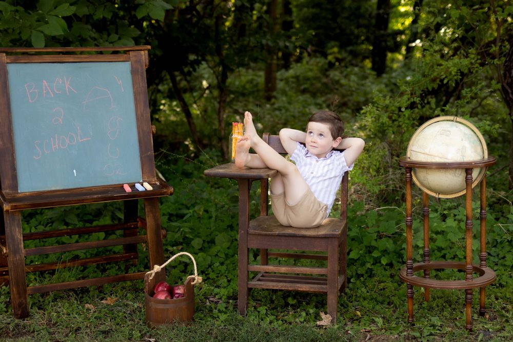 A vintage school desk setup with chalkboard and globe in an outdoor woodland setting.