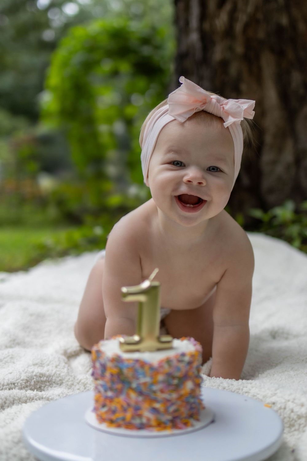Baby wearing pink headband with first birthday cake and gold number one candle.