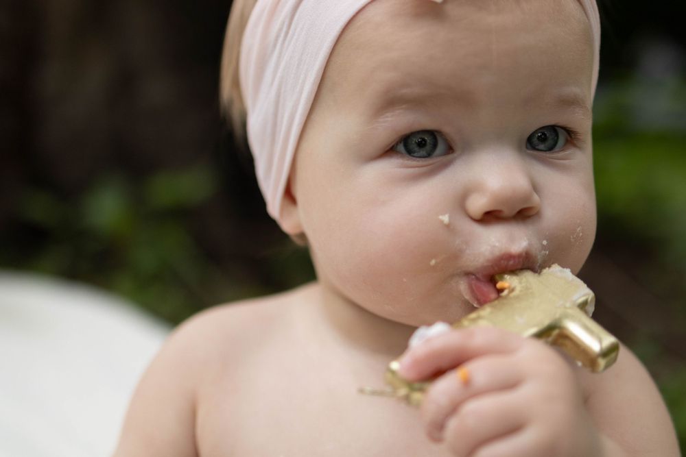 Baby in pink headband eating gold birthday cake frosting.