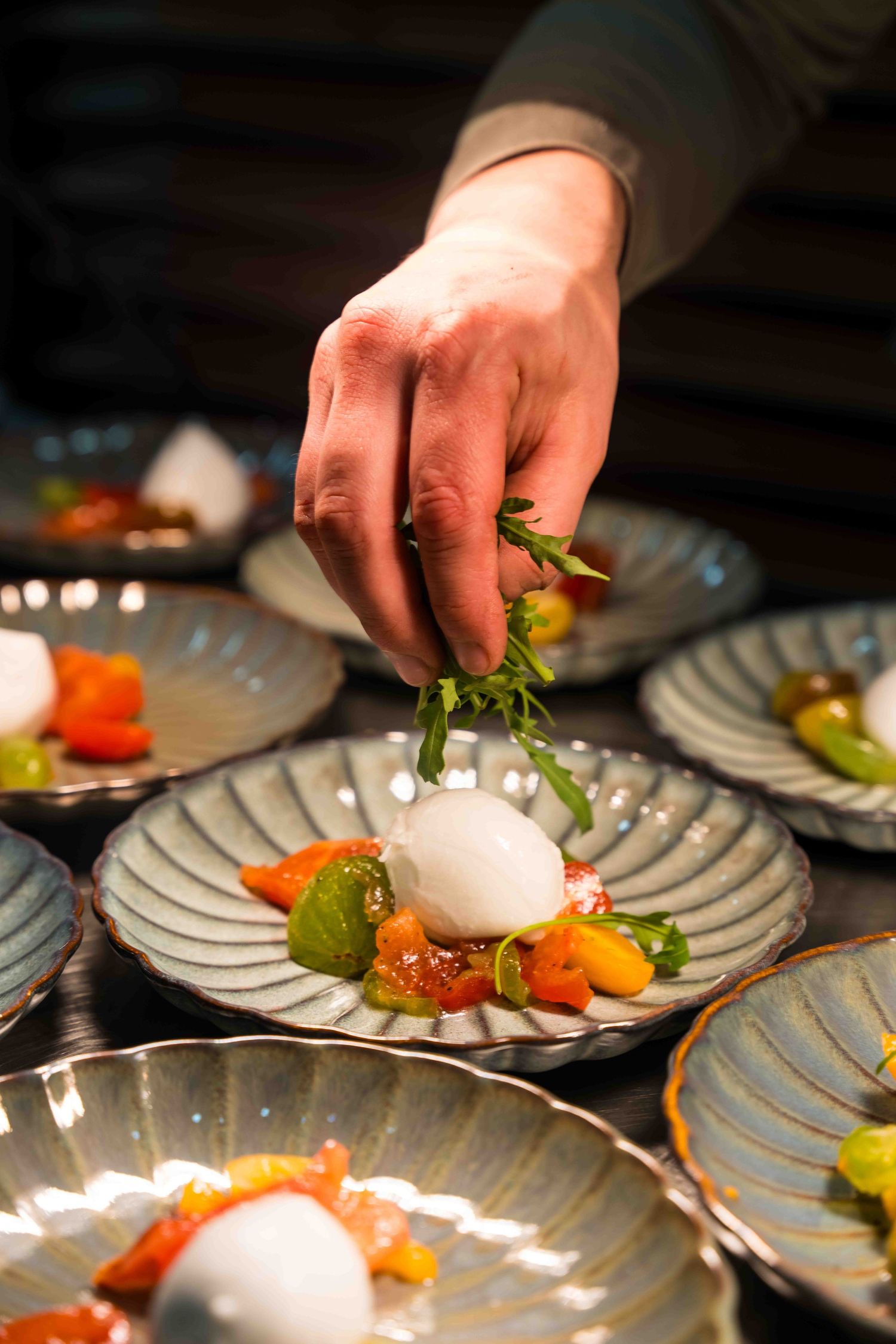 Chef's hand garnishing an elegant plated dish with microgreens and white spheres.