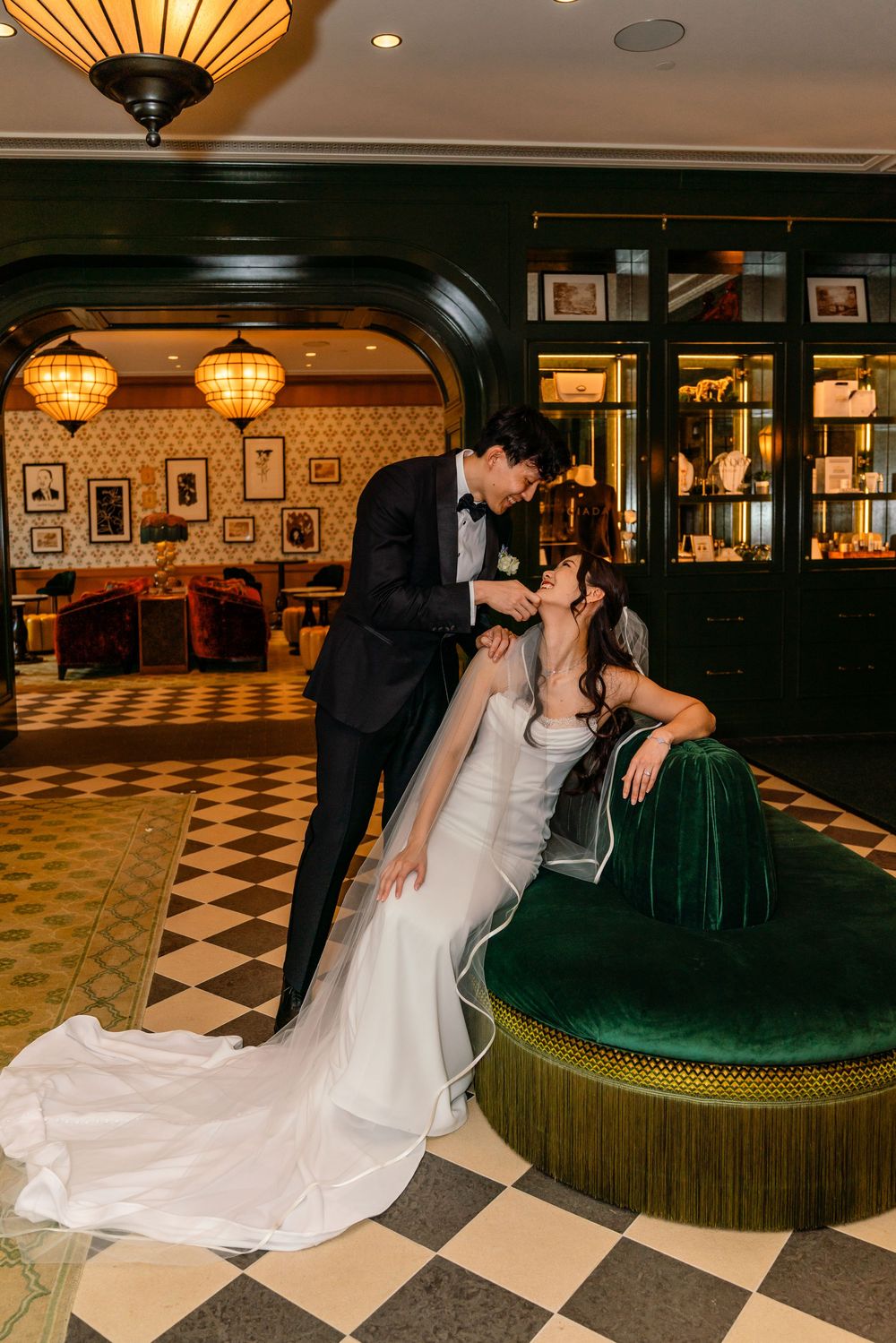 Bride and groom share a romantic moment in an elegant venue with green velvet seating and checkered floors.