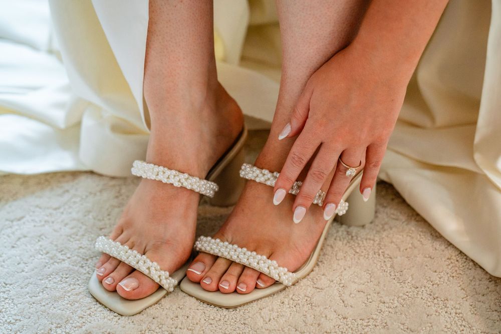Close-up of bride wearing pearl-embellished heeled sandals with elegant manicured nails and a diamond ring.