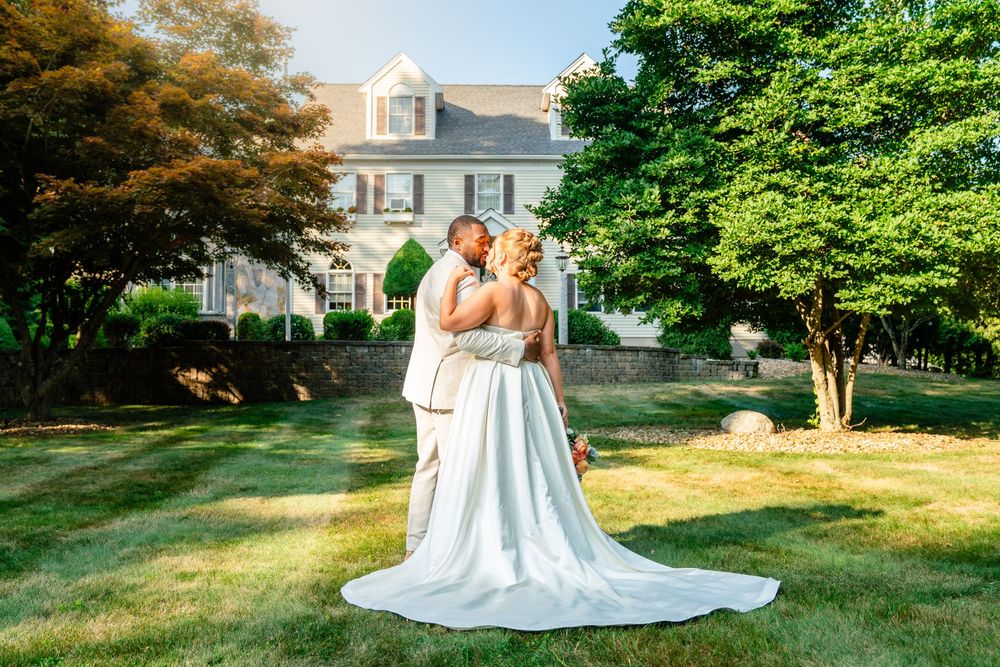 Bride and groom share a romantic kiss on a lush green lawn in front of an elegant estate on their wedding day.