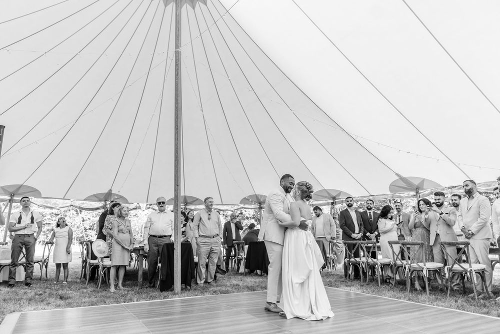 Couple shares first dance under elegant sperry tent at outdoor wedding reception with seated guests.