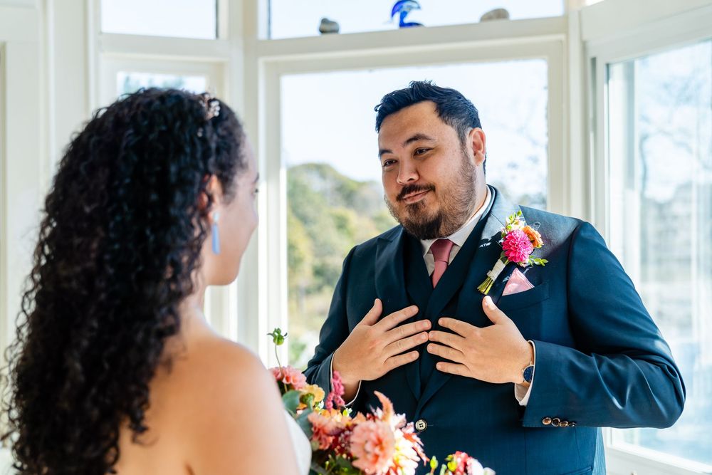 Groom in navy suit with pink boutonniere reacts emotionally during first look with bride at wedding.