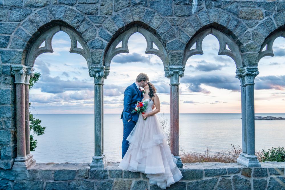 Wedding couple embracing in gothic stone arches overlooking ocean vista.