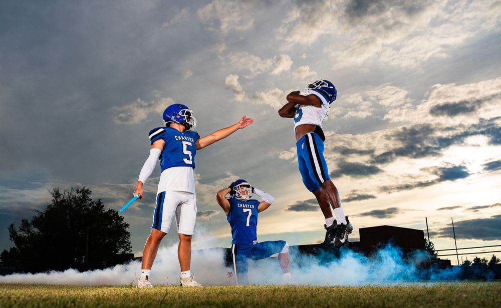 Two soccer players perform an acrobatic flip kick move against a dramatic cloudy sky during sunset.