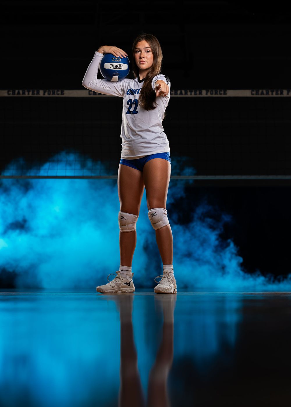 A volleyball player strikes a powerful serving pose against a dramatic backdrop of blue smoke.